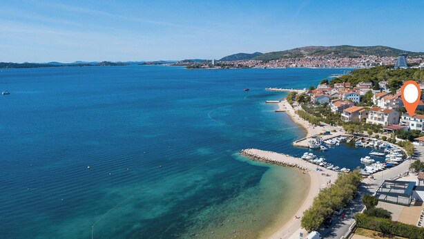 Une ville côtière dotée d’un port de plaisance, d’eaux d’un bleu limpide et d’un paysage vallonné en arrière-plan.