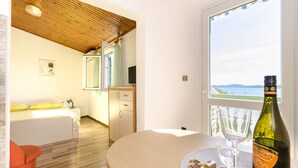 Une chambre moderne avec un plafond en bois, un lit avec des oreillers jaunes, une petite table avec une bouteille de vin et des verres, et une vue sur la mer par la fenêtre.