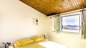 Une chambre à coucher comprenant un lit, des tables de chevet, une lampe de chevet, une fenêtre avec des rideaux et une vue sur la mer.