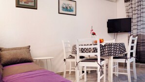 Una habitación con una cama, una mesa de comedor con sillas, un televisor y dos cuadros en la pared.
