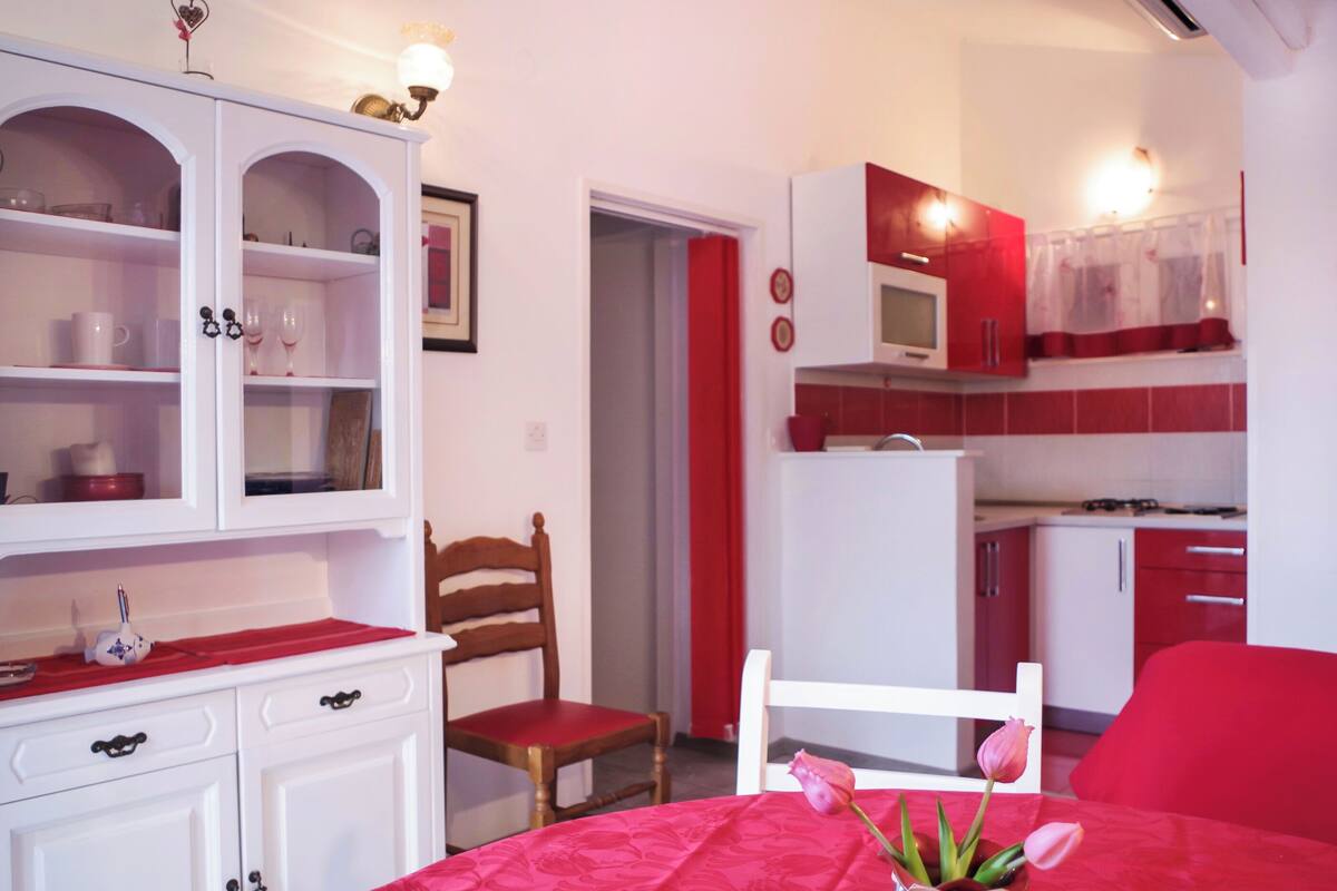 A compact kitchen with white cabinets, a red dining area, and a small table with a vase of flowers.
