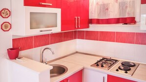 Una cocina compacta con armarios rojo y blanco, un microondas, un lavamanos y una estufa a gas.