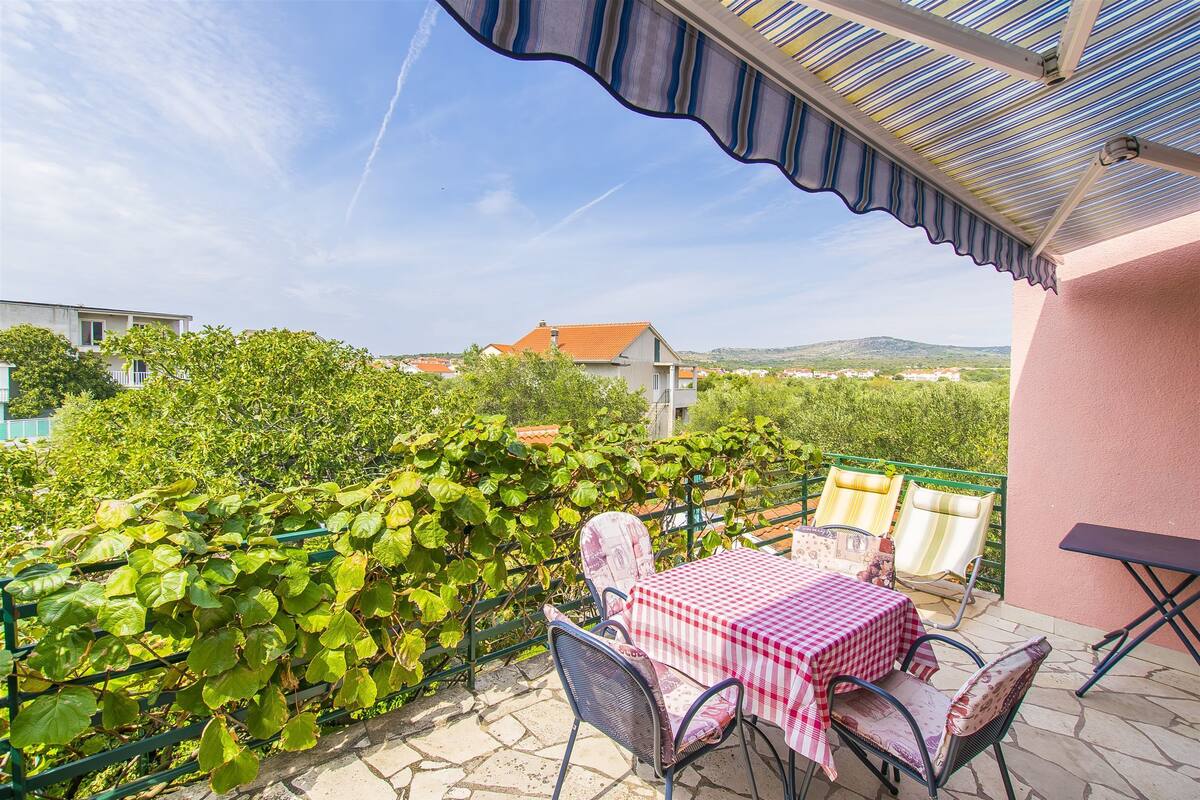 A patio with a table and chairs, a view of a vineyard, and a building in the background.