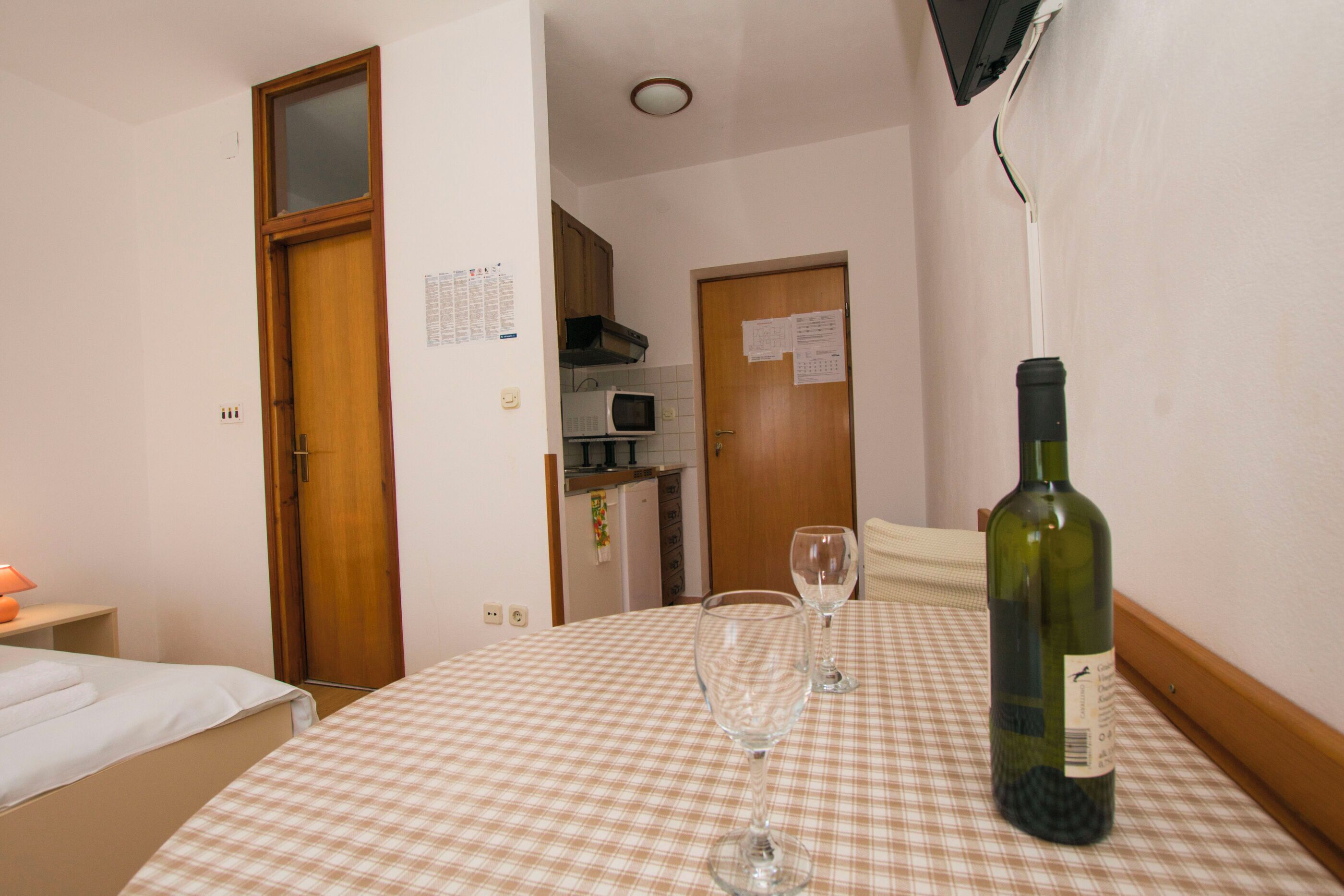 A hotel room with a checkered tablecloth, a bottle of wine, and two wine glasses.