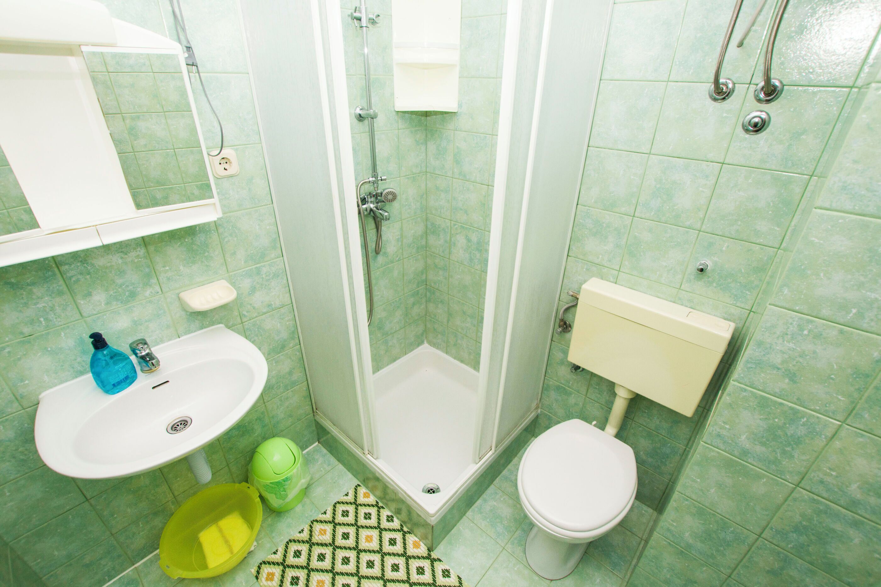 A bathroom with a shower, sink, toilet, and a mirror.