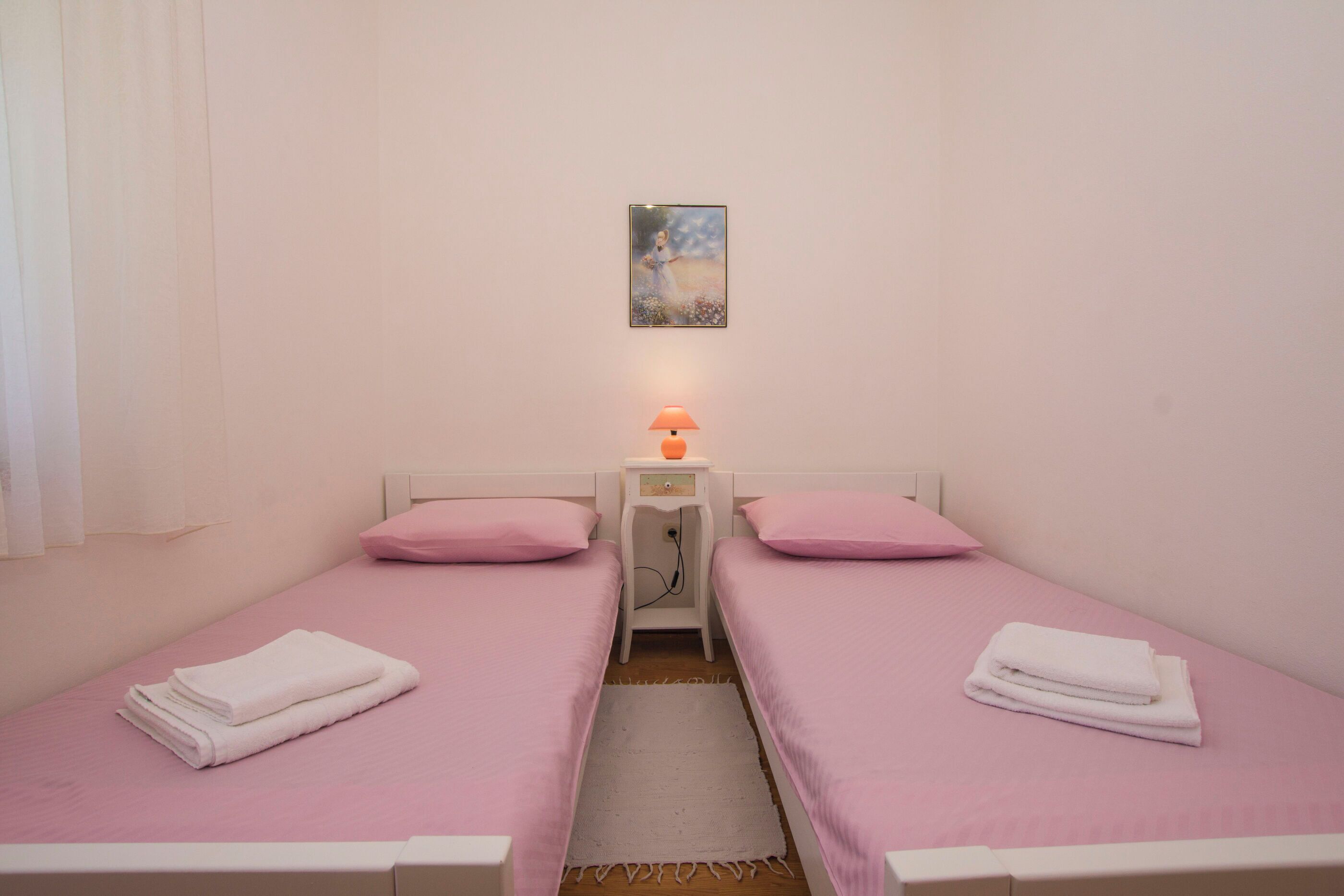 Ein kleines, sauberes Zimmer mit zwei Einzelbetten, einem Nachttisch mit Lampe und einem Bild an der Wand.