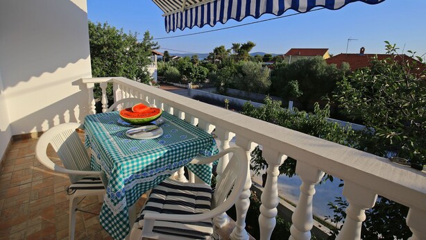 A balcony with a checkered tablecloth, a bowl of watermelon, and a striped cushion. - Apartments Verica (Sukosan)