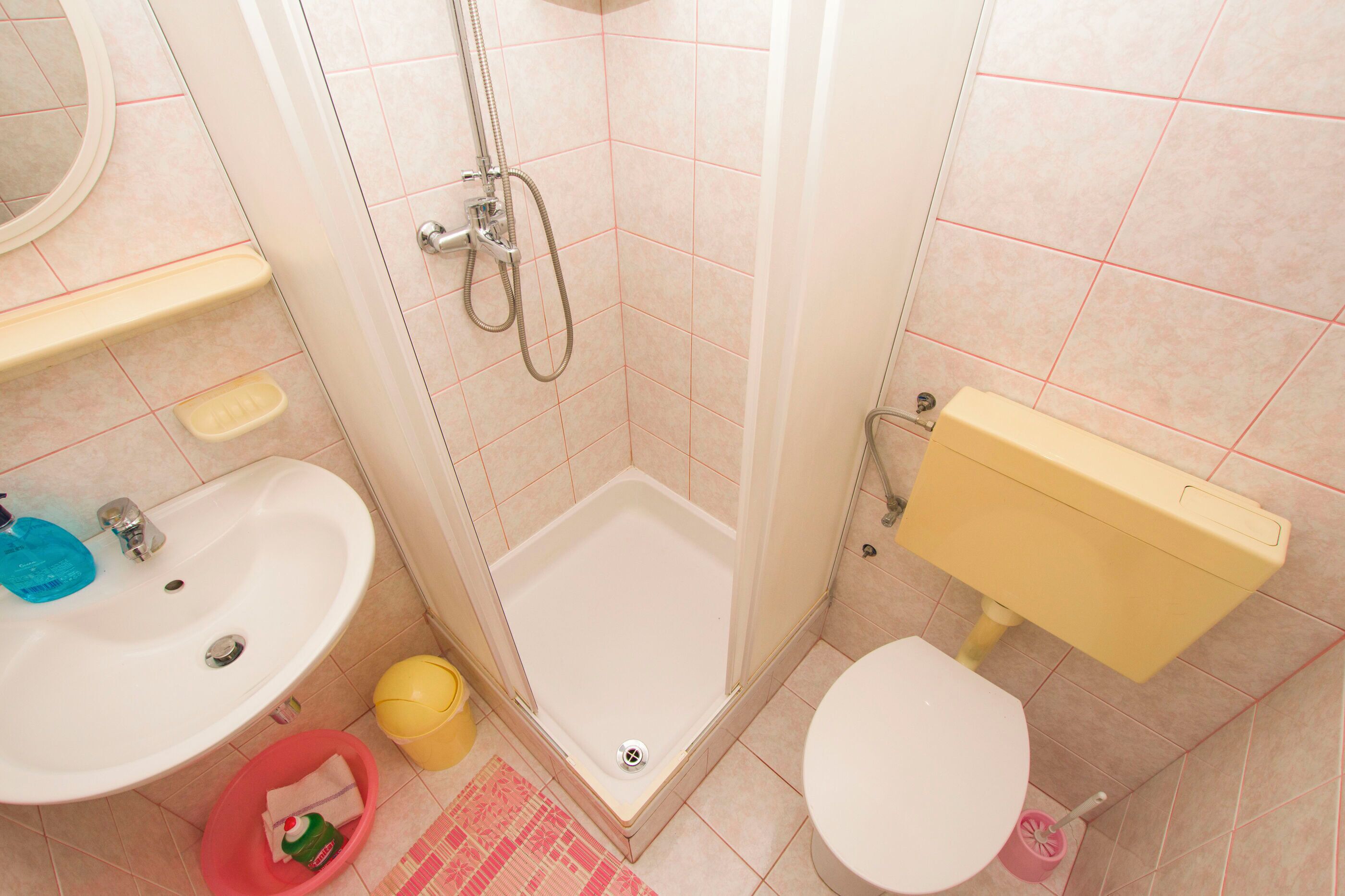 Een badkamer met douche, toilet, wastafel en een klein prullenbakje.