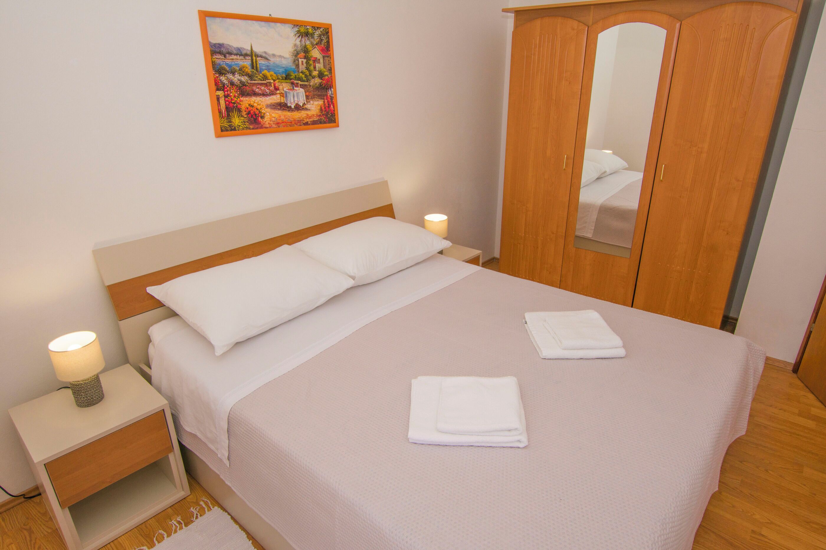 Una cama bien hecha con sábanas blancas, una lámpara de noche y una toalla doblada sobre la cama.
