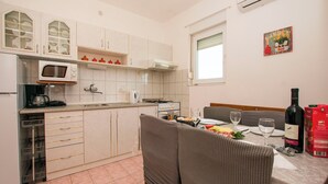 A compact kitchen with a microwave, stove, and sink. There is a dining area with a table set for two, a wine bottle, and a box of cereal. - Apartments Verica (Sukosan)