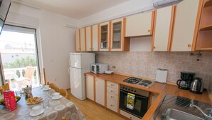 A compact kitchen with wooden cabinets, a refrigerator, a microwave, a stove, and a sink. - Apartments Verica (Sukosan)