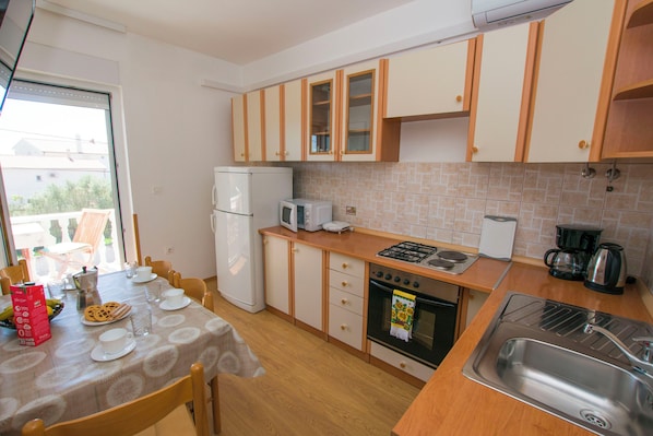 Een kleine keuken met houten kastjes, een koelkast, een magnetron, een fornuis en een spoelbak.