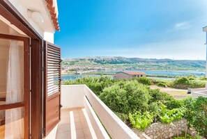 A balcony with a view of a lake, greenery, and distant hills. - Apartments Mate (Pag)