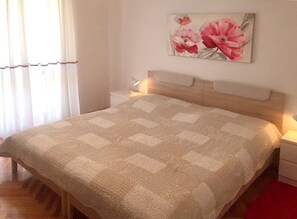 Ein Schlafzimmer mit einem Bett, einem Nachttisch, einer Lampe und einem Blumenbild an der Wand.
