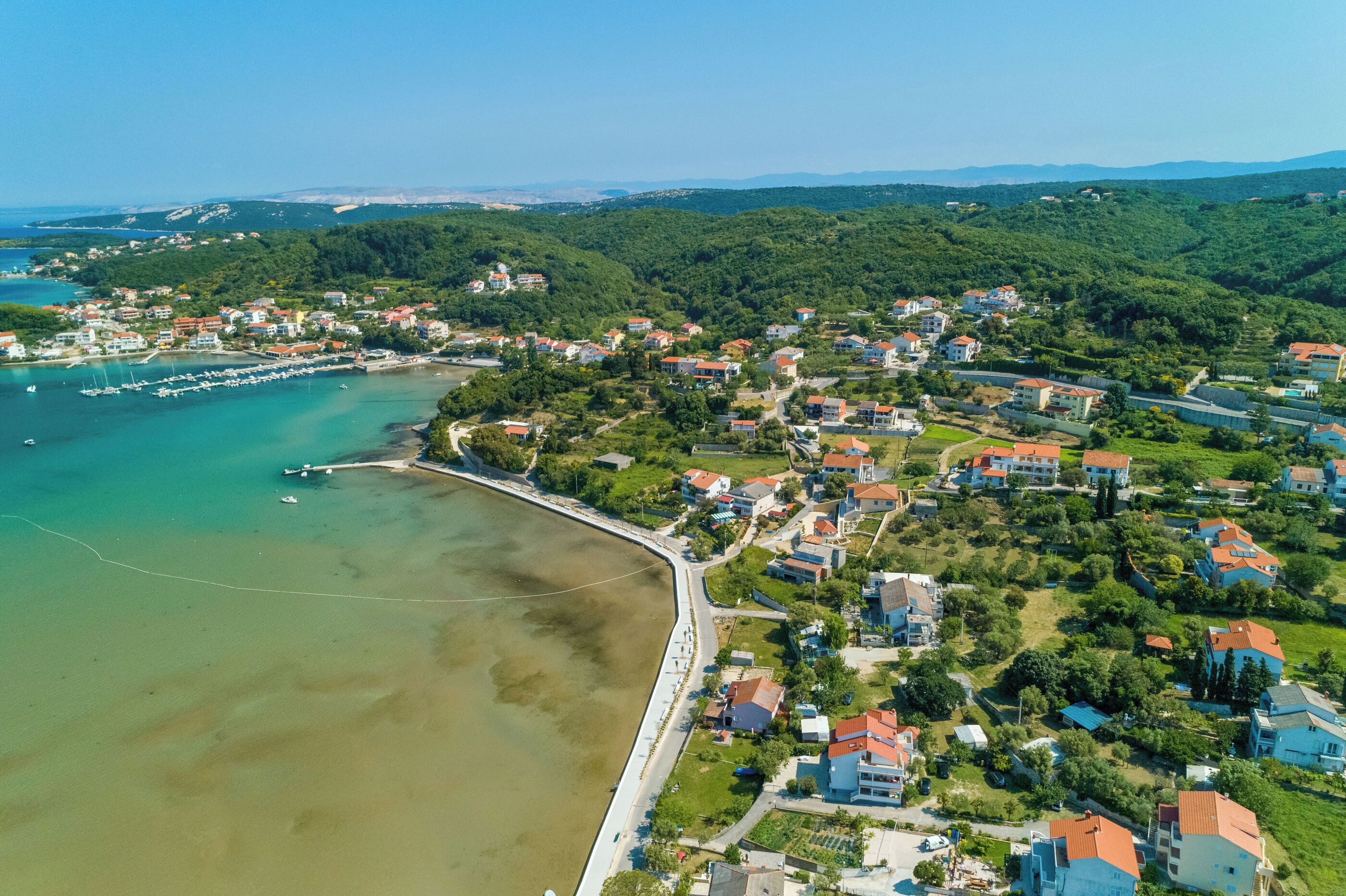 Vista aérea de un pueblo costero con casas, un puerto deportivo y una playa.