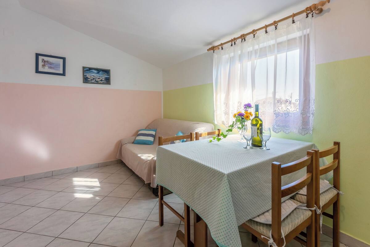 A dining area with a table set for two, a sofa, and a window with curtains.