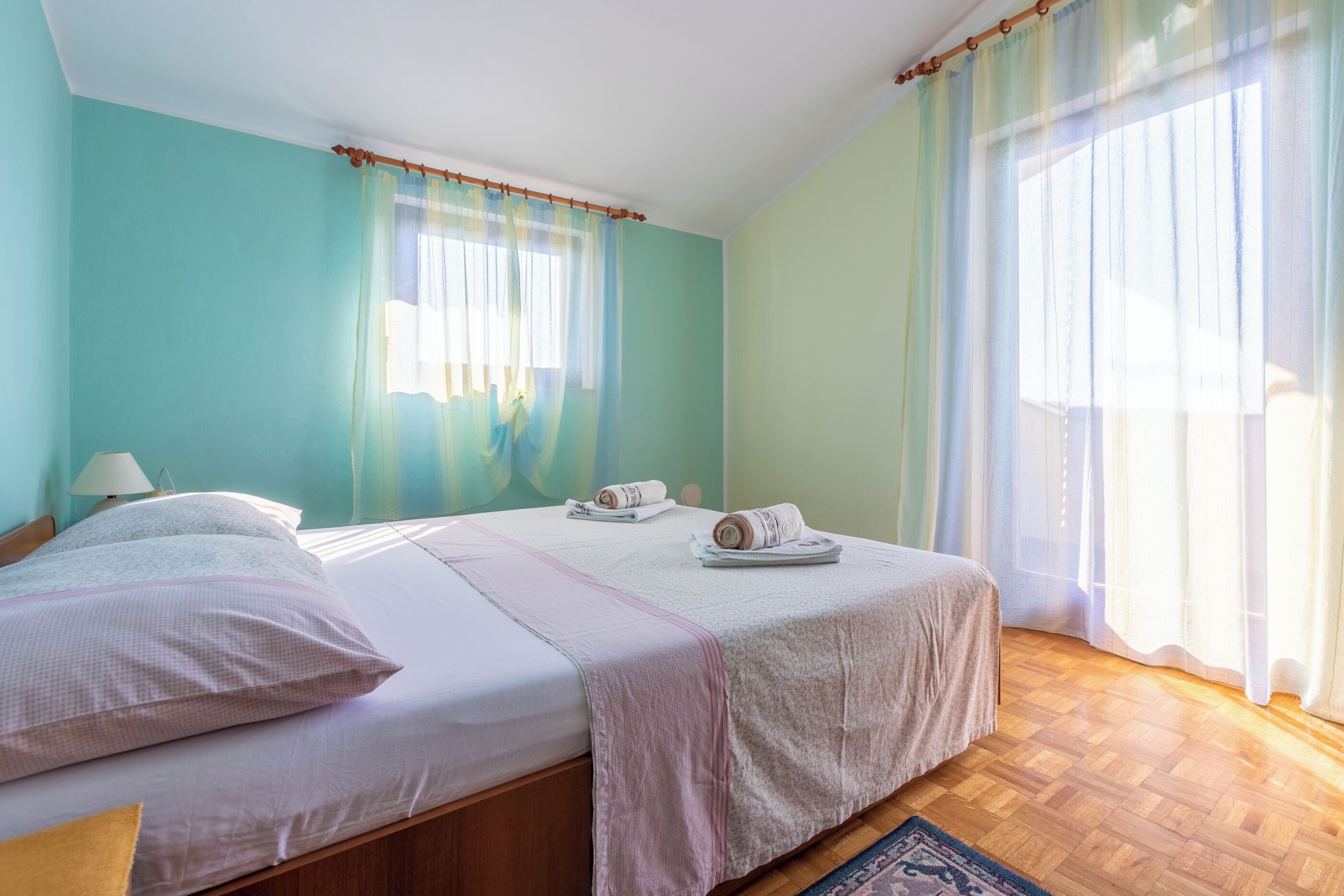 A bedroom with two beds, a wooden floor, and a window with sheer curtains.