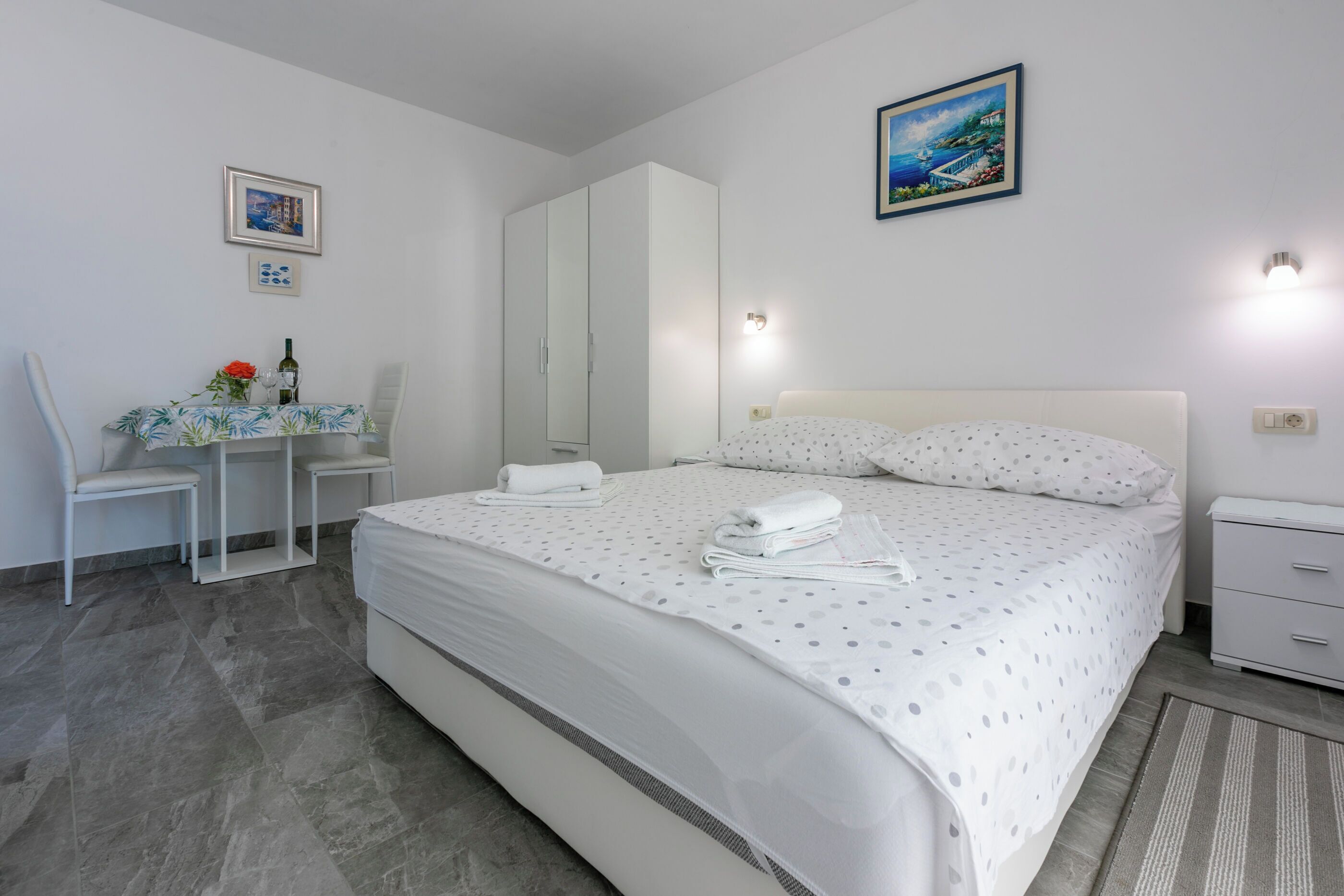 Un dormitorio con cama, escritorio, silla, armario y un cuadro en la pared.