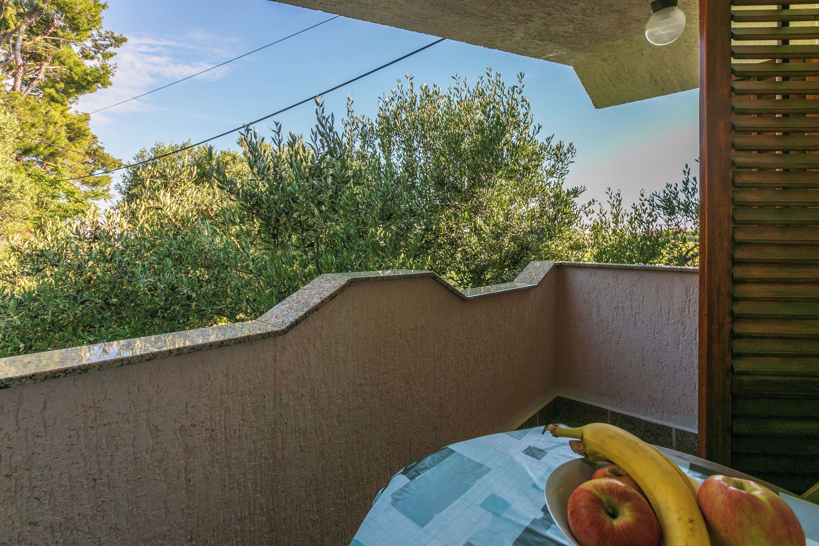 Ein Balkon mit einem Tisch, auf dem eine Banane, ein Apfel und eine Schüssel stehen.