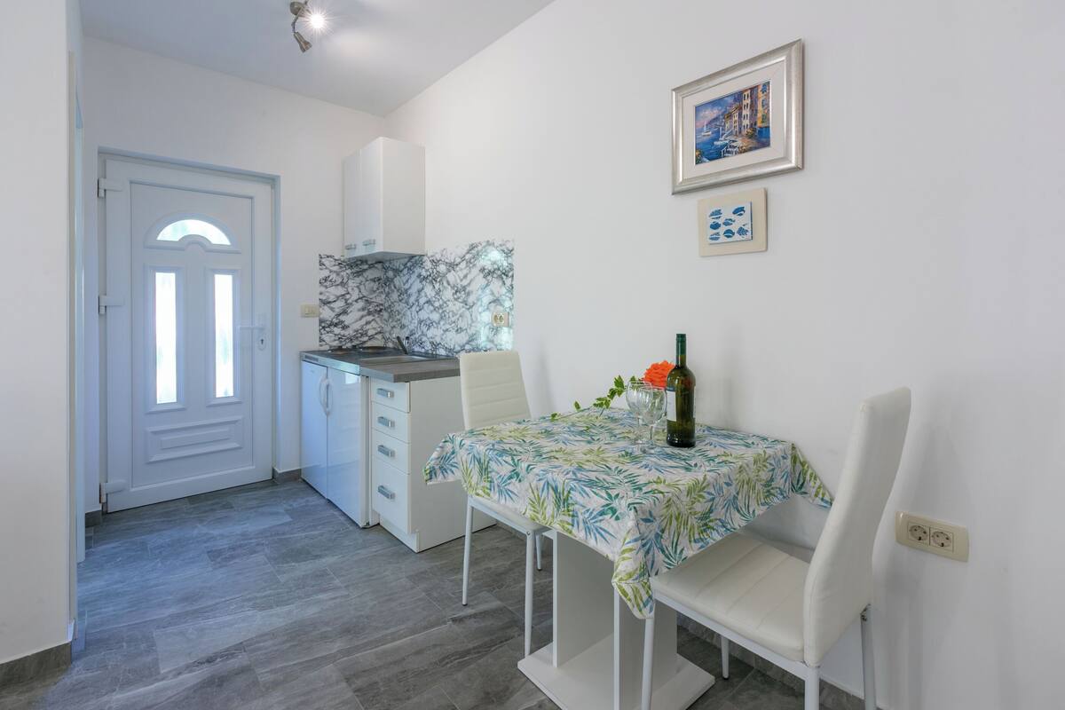 A compact kitchen with white cabinets, a marble backsplash, and a dining area with a table set for two.