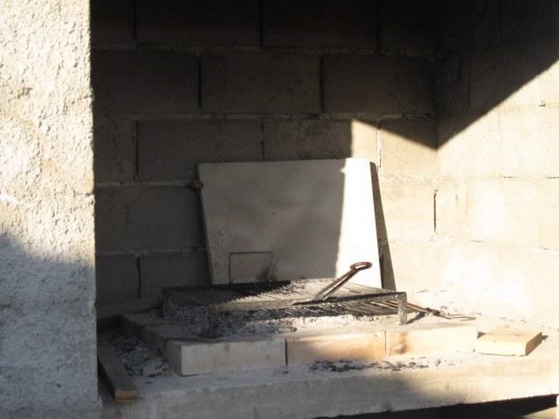 A concrete structure with a metal grate and a wooden plank leaning against it.