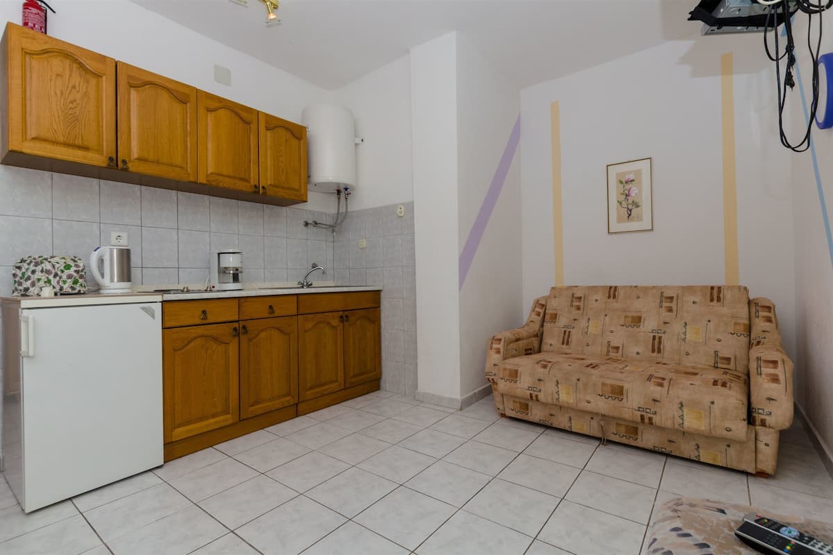 A compact kitchen with wooden cabinets, a white refrigerator, and a patterned sofa in a living area.