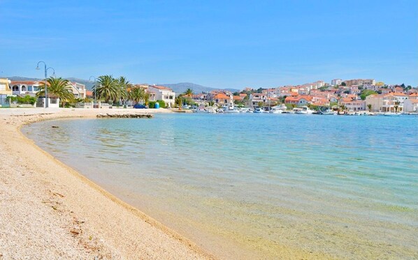 A coastal town with a sandy beach, clear water, and buildings in the background.