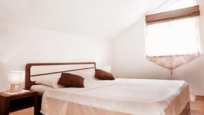 A neatly made bed in a room with a sloped ceiling and a window with a sheer curtain. - Apartment Sunset (Vodice)