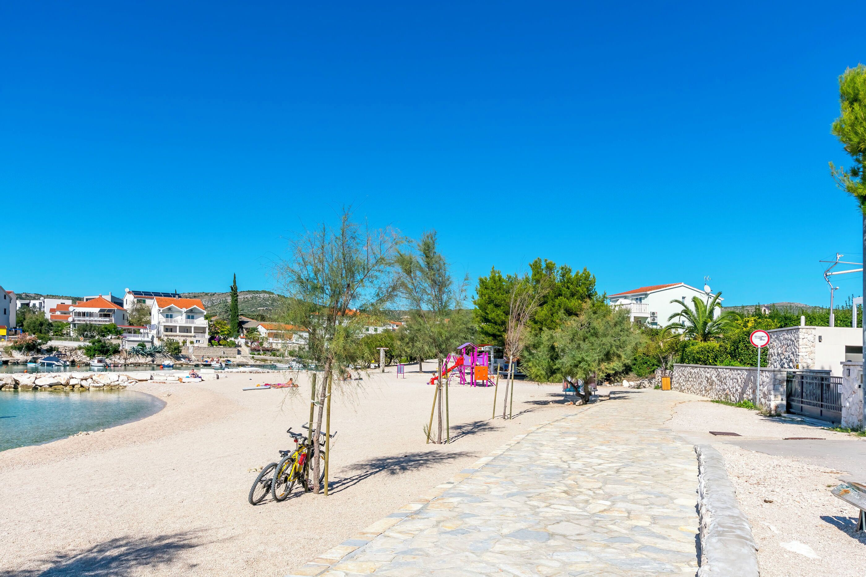 A coastal area with a paved walkway, bicycles, and a playground.
