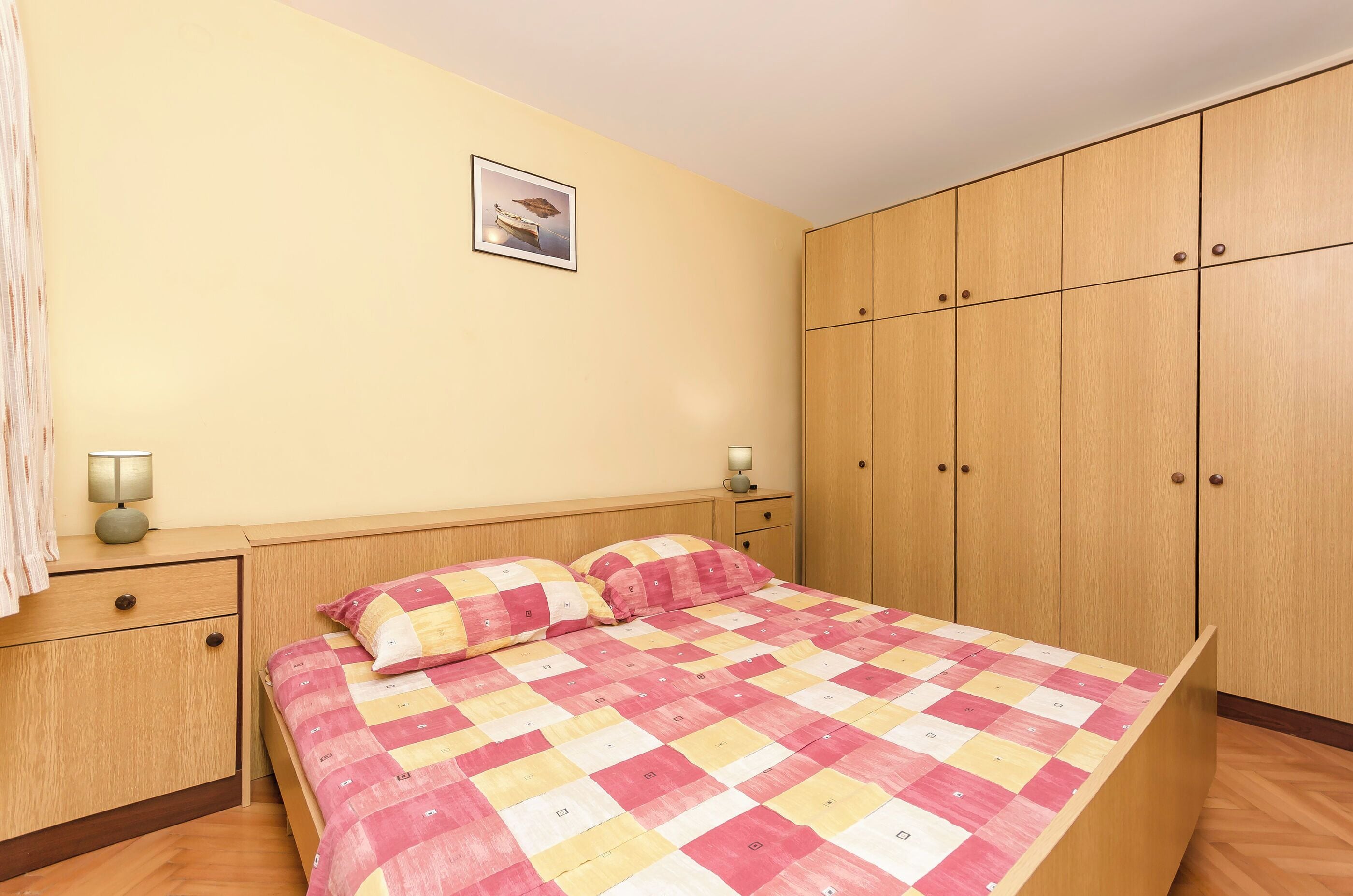 Une chambre à coucher avec un lit, une armoire en bois, des tables de chevet et un tableau encadré au mur.