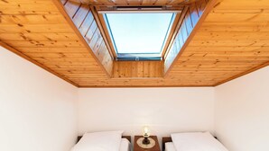 Une chambre avec une lucarne, deux lits et une table de chevet avec une lampe.
