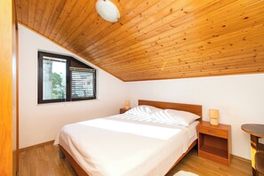 A bedroom with a wooden ceiling, a bed with white bedding, a nightstand with a lamp, and a window with blinds. - Apartments Green Garden (Vodice)