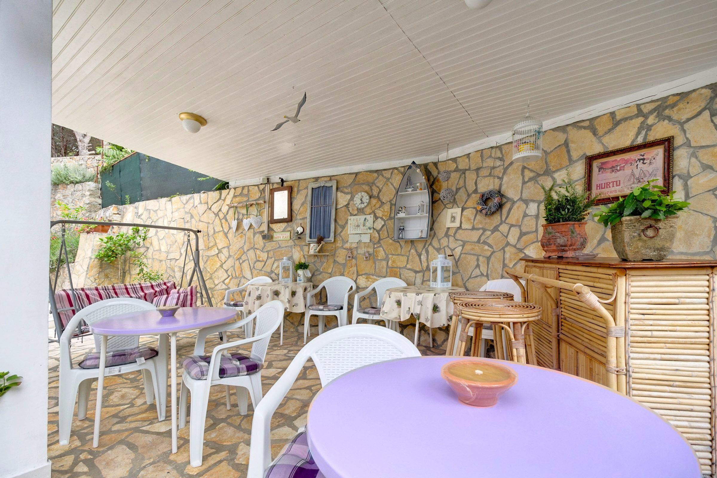Eine Terrasse mit Steinmauern, weißen Korbmöbeln und einer kleinen Bar.