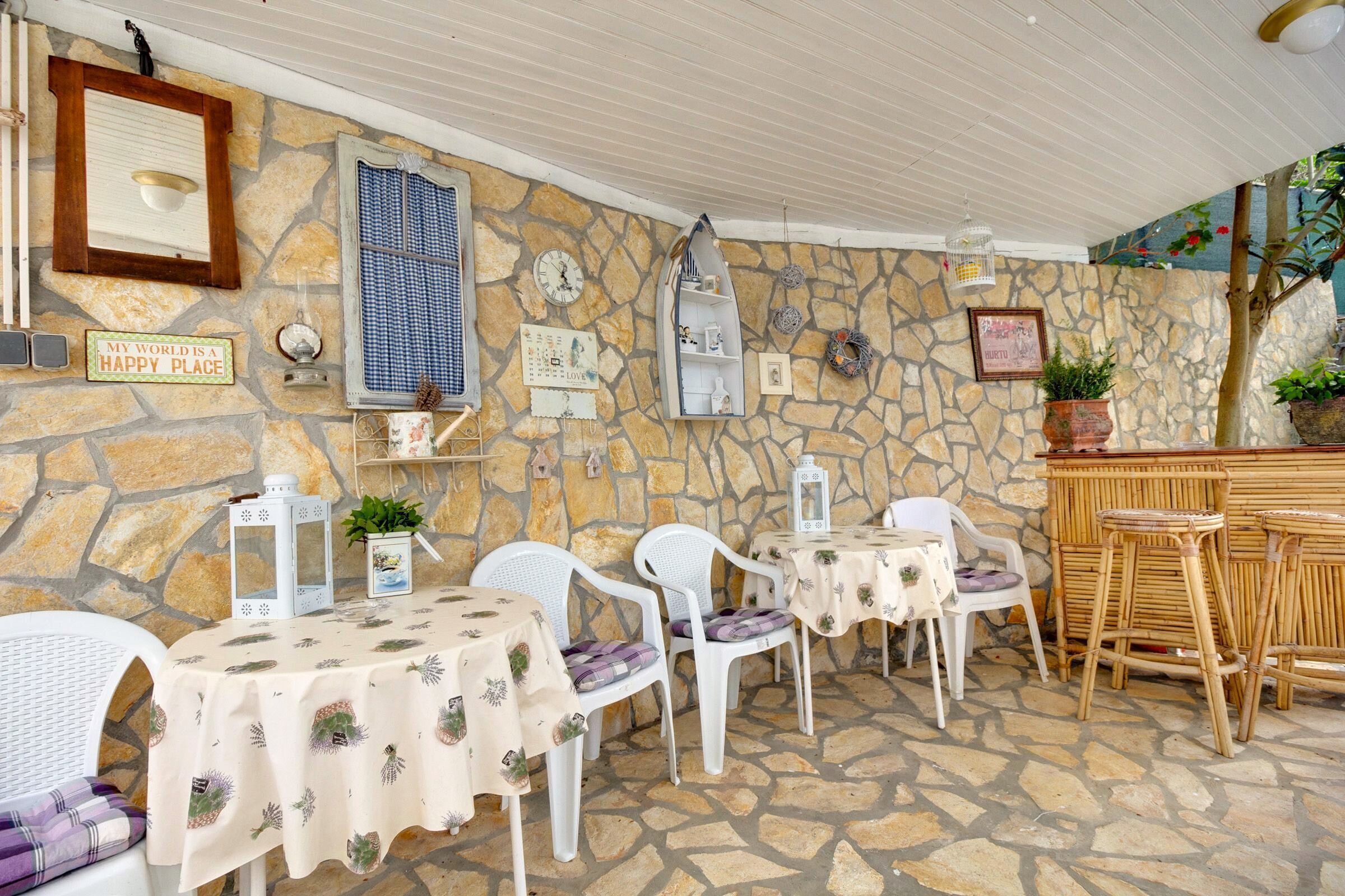 Un espace extérieur aménagé en terrasse, avec des murs en pierre, des meubles en osier blanc et des tables recouvertes de nappes à motifs floraux.