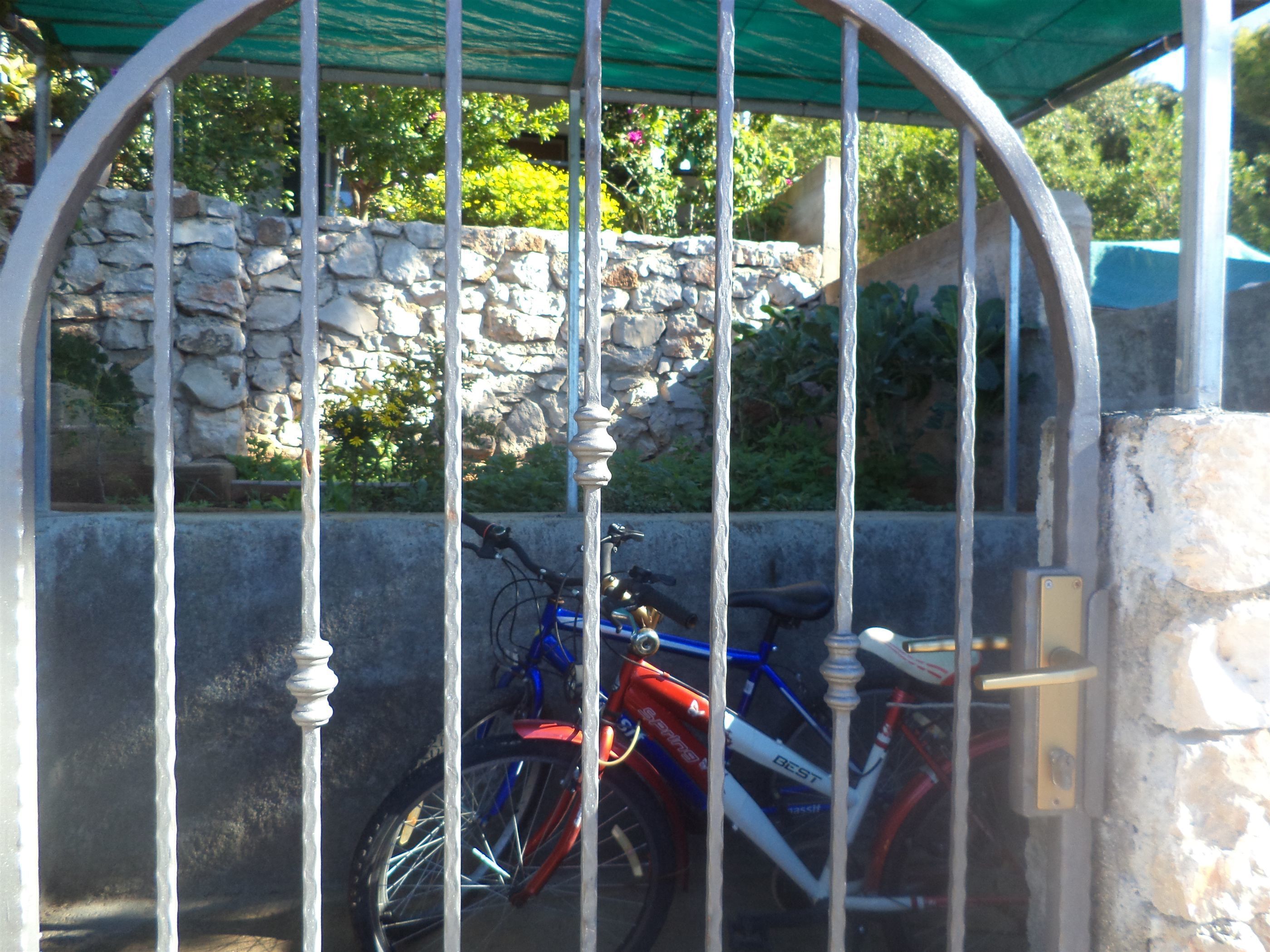 Un espace de stationnement pour vélos sécurisé, délimité par un mur en pierre et une porte en métal.
