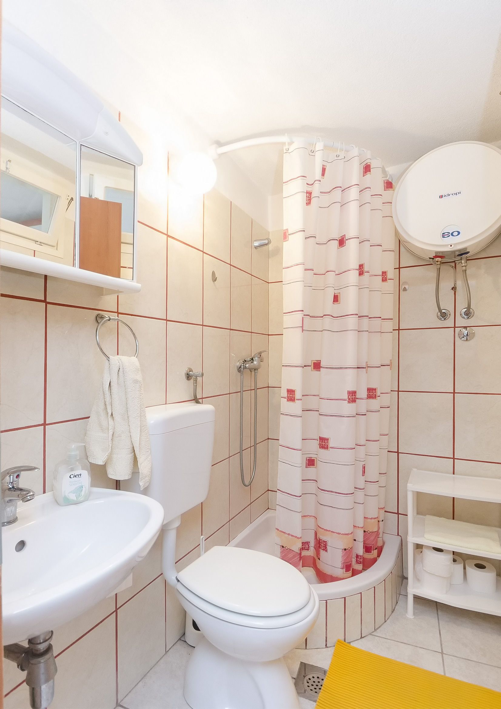 A bathroom with a toilet, sink, shower, and a mirror.