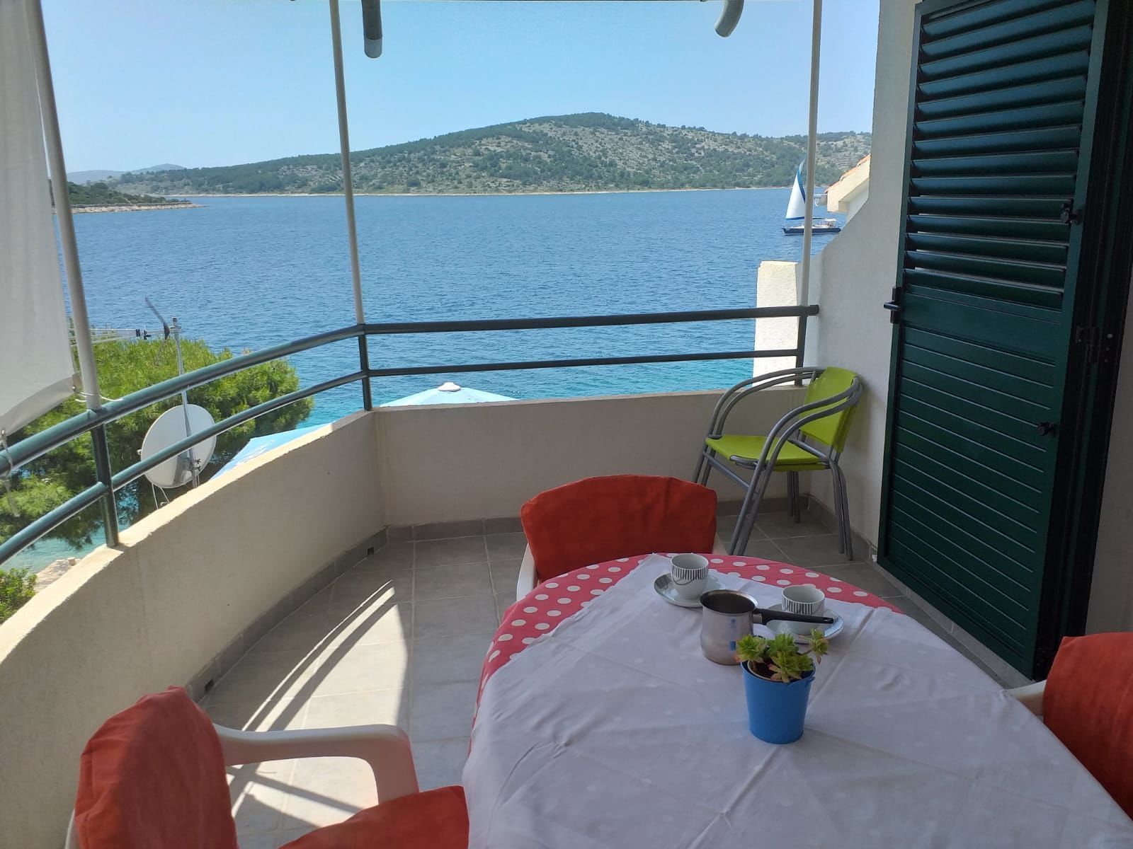 Ein Balkon mit Tisch für zwei Personen, Blick auf ein Gewässer und eine entfernte Hügelkette.