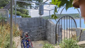 Une structure en béton avec une porte en métal, un vélo, et une vue sur une étendue d’eau et des collines en arrière-plan.