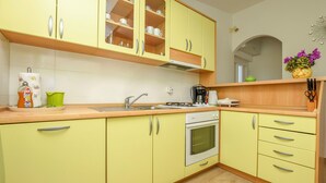 Een keuken met gele kastjes, een spoelbak, een fornuis en een koffiezetapparaat.