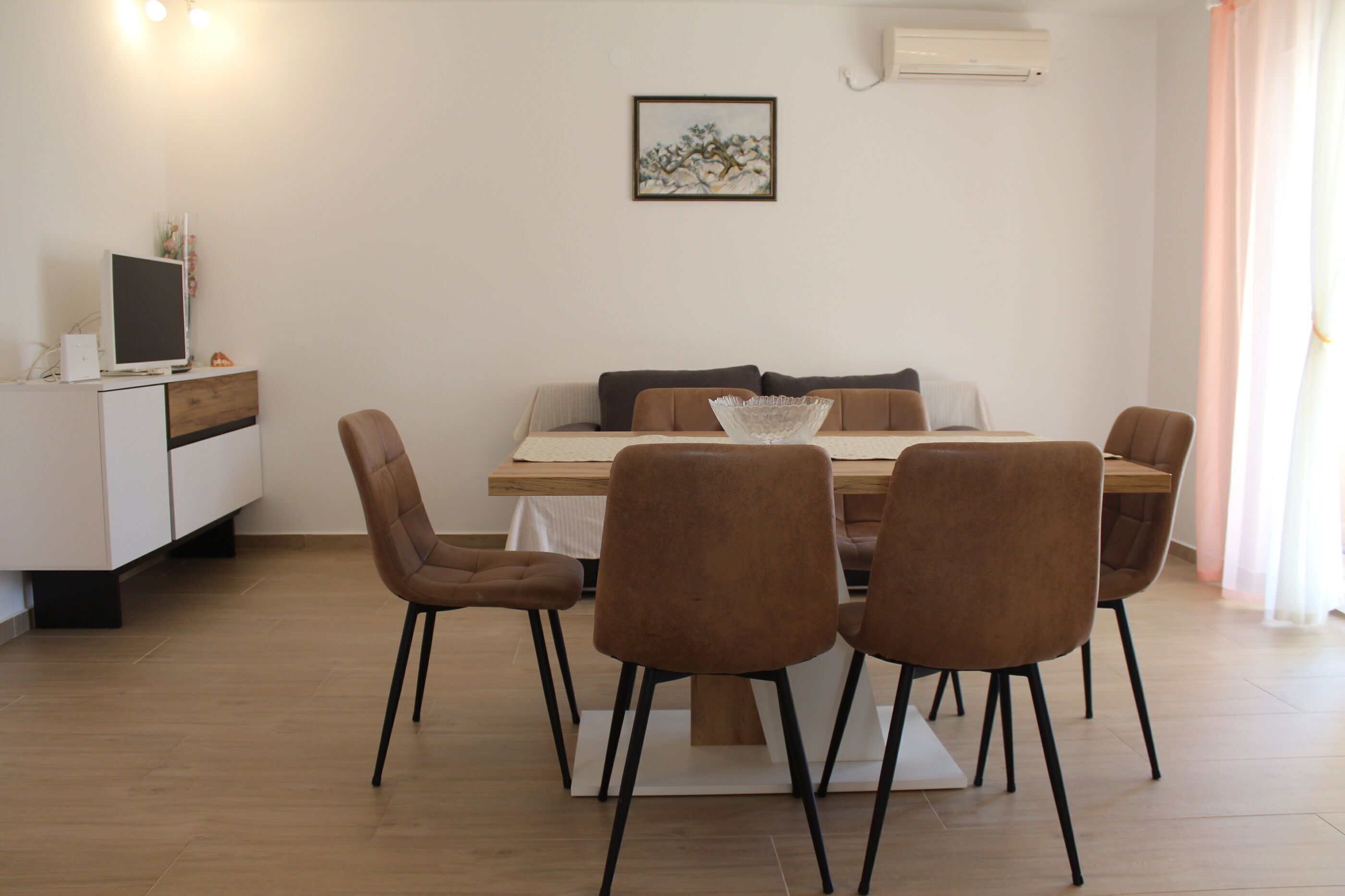 A dining area with a wooden table, four brown chairs, a white cabinet, and a framed picture on the wall.