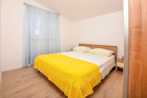 A bedroom with a bed, a nightstand, a lamp, and a window with curtains. - Apartments Branko (Rogoznica)