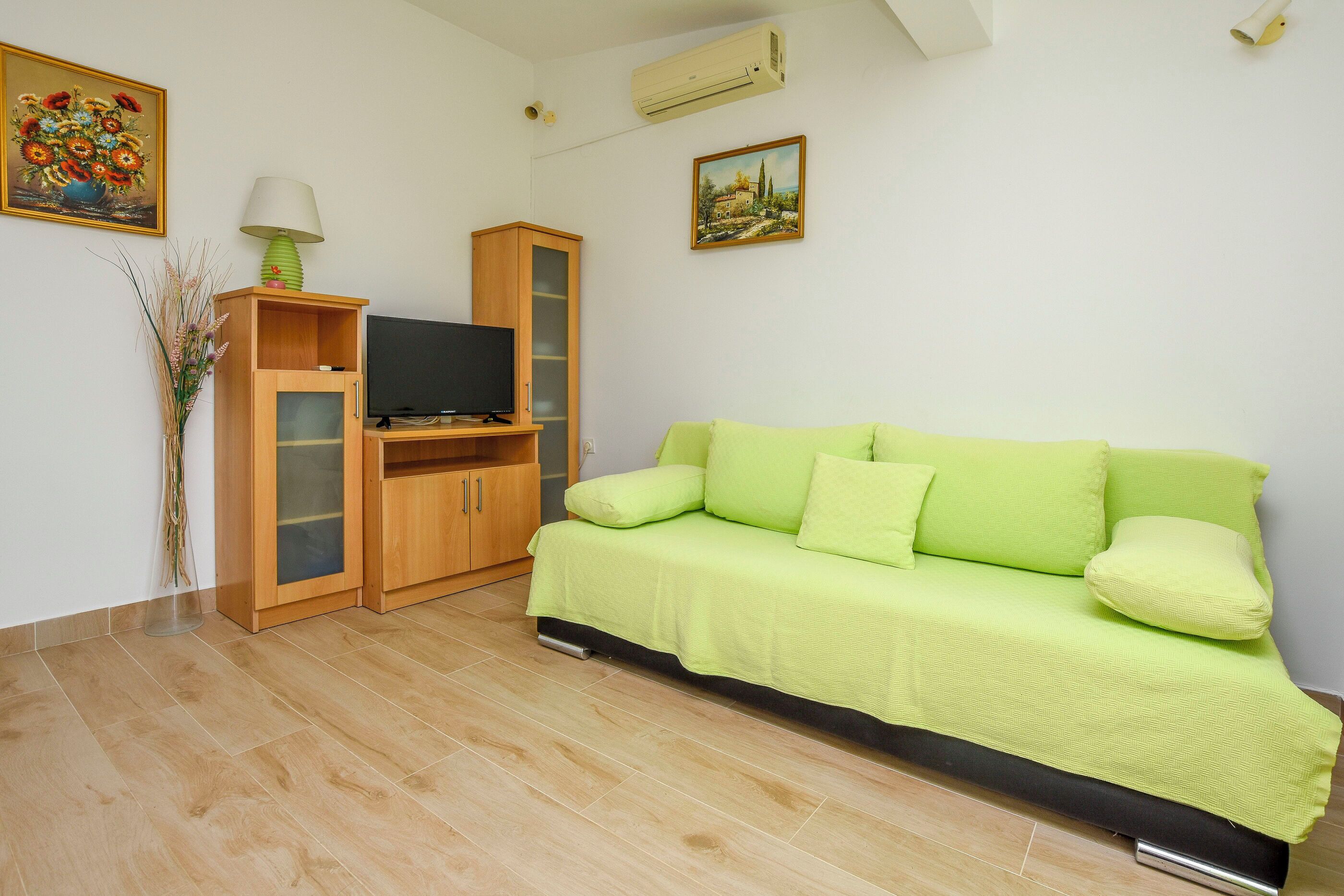 A living room with a green sofa, a wooden cabinet, a television, and two paintings on the wall.