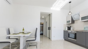 Una cocina moderna con comedor, que presenta una mesa blanca, armarios grises y un horno empotrado.