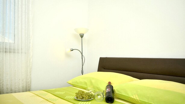 A bed with green bedding, a bedside lamp, a bottle, and a plate of grapes.