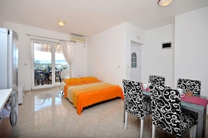 A hotel room with a bed, a dining table with chairs, a washing machine, and a view of the sea through the window. - Apartment Srima (Srima)
