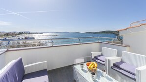 A balcony with wicker furniture, a table with fruits and drinks, and a view of the sea and boats.
