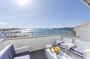 Un balcon agrémenté de meubles en osier, une table avec des fruits et des boissons, et une vue sur la mer et les bateaux.
