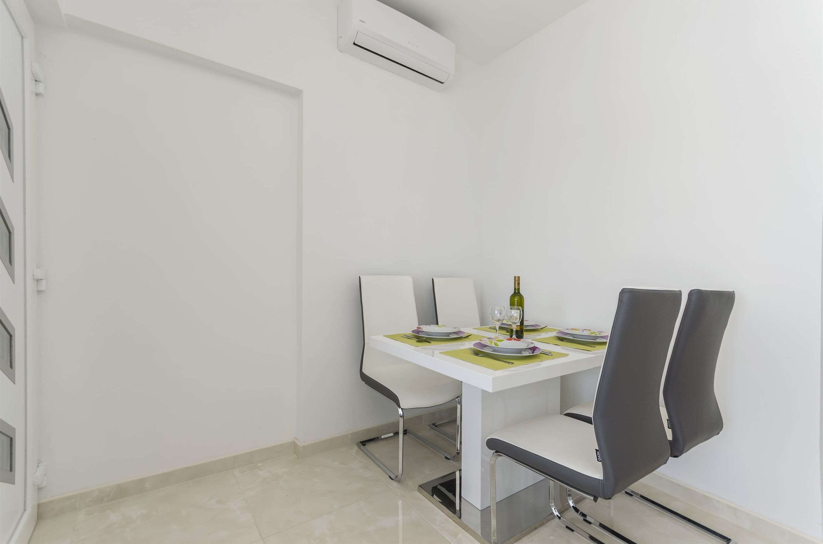 A dining area with a white table, grey chairs, and a bottle of wine.