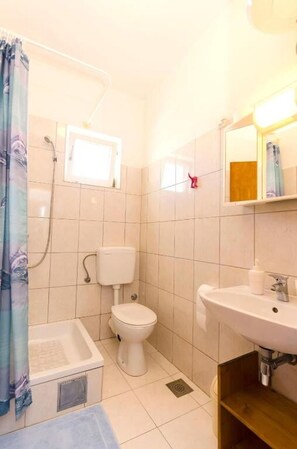 Ein Badezimmer mit Dusche, Toilette, Waschbecken und einem kleinen Fenster.