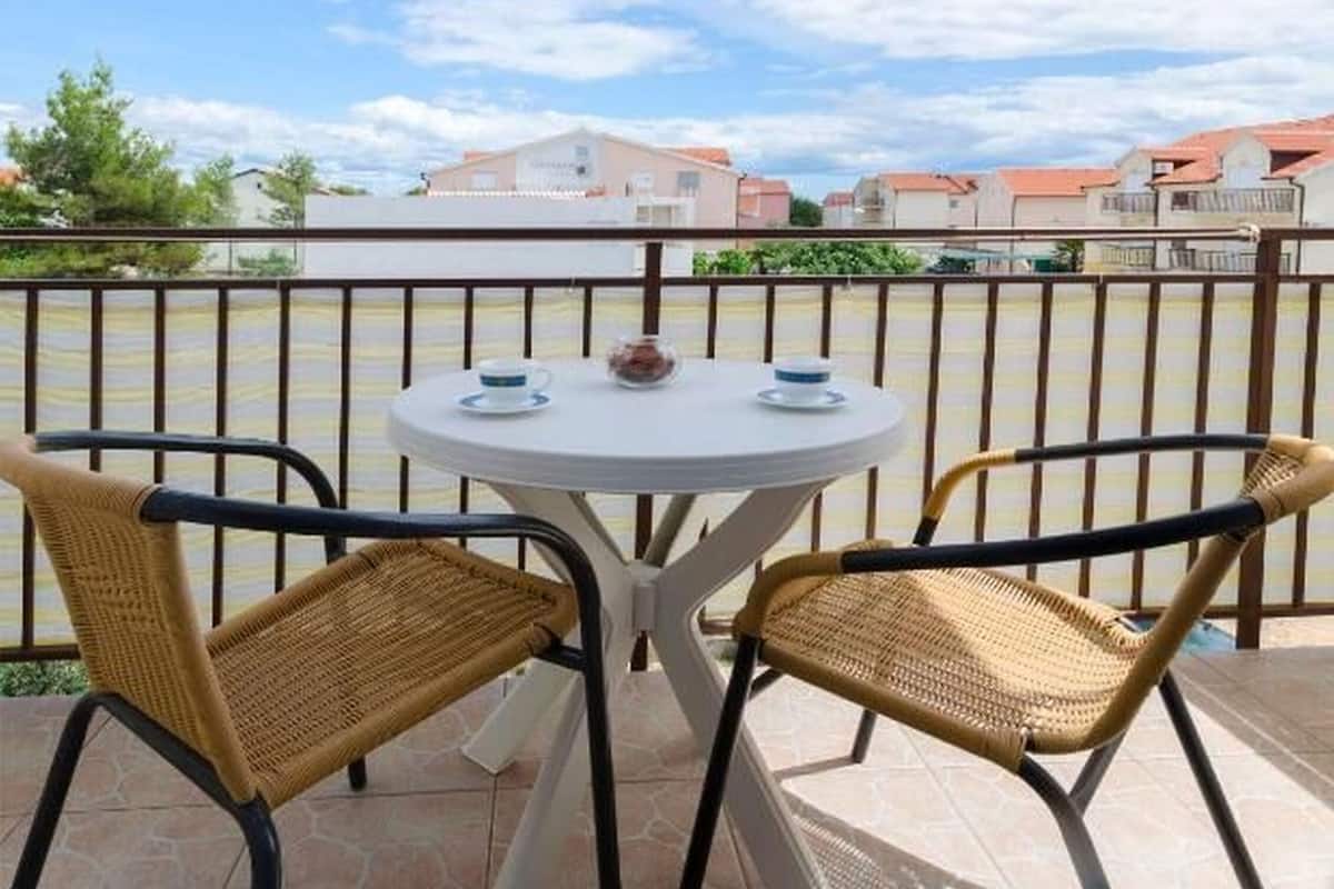 A round table with two wicker chairs, a white tablecloth, and a small white table with two cups and a glass.
